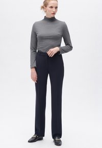 Grå polokrage topp kombinerad med höga midje byxor i marinblått. Byxorna har en skräddarsydd passform och ett mjukt tyg, kompletterat av svarta loafers.