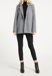 Manteau gris croisé en mélange de laine avec revers crantés, poches latérales et coupe décontractée, porté avec un pantalon noir slim et des bottines.