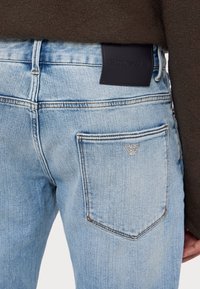 Light blue denim jeans with a slim fit. Features a black leather label at the back waist and a small embroidered logo on the right pocket.