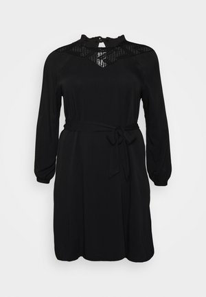 Zwarte jurk met lange mouwen en een strikceintuur. Heeft een kanten halslijn en gladde stof. Eenvoudige, rechte snit met een bescheiden ontwerp.