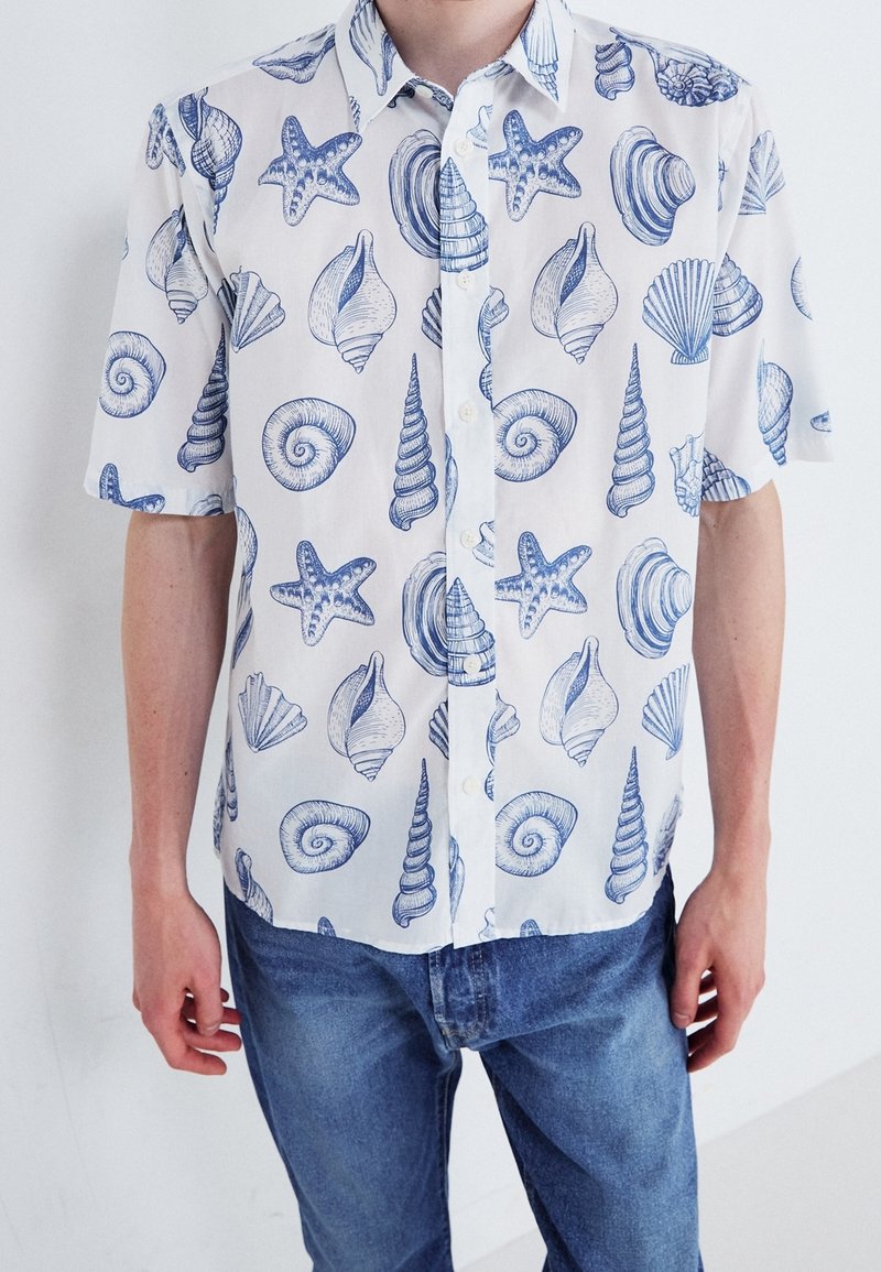 Košile s krátkým rukávem s bílým pozadím a modrými vzory mušlí a hvězdic. Vyrobeno z lehkého materiálu s volným střihem.