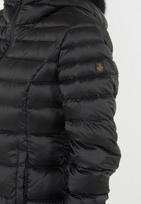 Giubbino nero imbottito con design a righe orizzontali, chiusura con zip e cappuccio foderato in pelliccia. Presenta un logo del marchio sulla manica sinistra.
