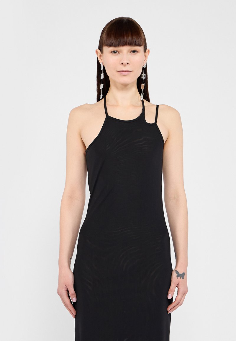 Robe noire à col halter avec des bretelles fines, présentant une silhouette ajustée et une texture subtile. Le mannequin porte des boucles d'oreilles géométriques en argent et a les cheveux raides.