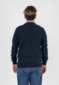 Felpa a maniche lunghe blu navy con colletto rotondo e polsini a costine, abbinata a jeans in denim azzurro. Tessuto liscio, senza motivi.