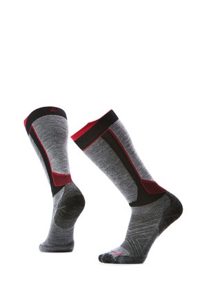 Par de calcetines grises hasta la mitad de la pantorrilla con detalles en negro y rojo, mostrados sobre formas de pie invisibles sobre un fondo blanco.