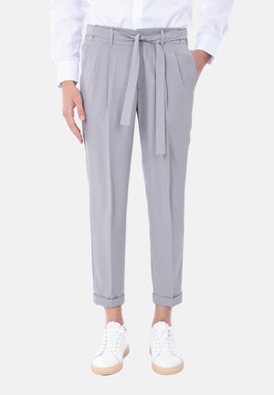 Pantaloni grigi chiari su misura con cintura, pieghe e risvolti, abbinati a sneakers bianche con suole in gomma color nocciola.