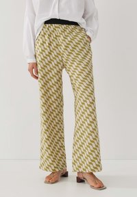 Vidbyxlade byxor i krämfärg med olivgröna vågmönster, med en elastisk svart midja och lättviktsmaterial.