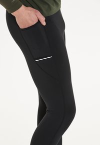 Svarta träningsleggings av elastiskt tyg, med en sidoficka med en vit accentrand och platta sömmar för komfort.