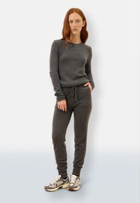 Szary sweter z dzianiny i pasujący zestaw dresowy o luźnym kroju, z elastycznym pasem i ściągaczami przy kostkach, zestawiony z sportowymi butami.