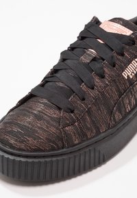 Baskets noires avec une tige texturée ornée d'accents en or rose, bout rond, semelle épaisse en caoutchouc et lacets plats noirs.