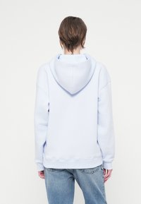 Hanorac albastru deschis cu glugă prevăzută cu șnur, croială lejeră și manșete ribbate. Purtați cu blugi din denim deschis, cu croială largă.