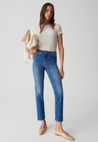 T-shirt a coste color beige chiaro, jeans in denim blu a vita alta e scarpe ballerine color nude. Modella con una borsa a tracolla crema, dal design semplice e dallo stile aderente.