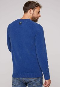 Maglione blu lavorato a maglia con polsini e orlo a coste, caratterizzato da un collo rotondo e un dettaglio testurizzato nella parte posteriore. Etichetta visibile all'apertura del collo.