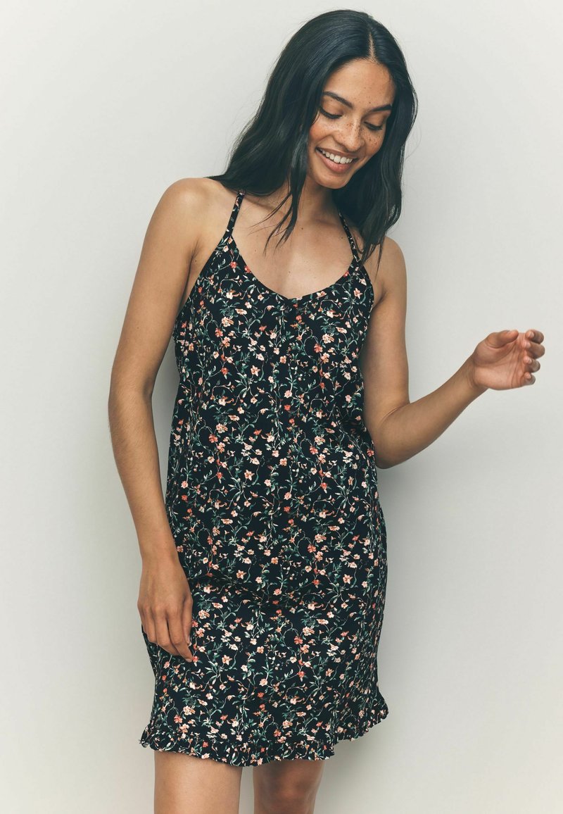 Vestido negro con flores, de tirantes finos, que presenta pequeñas flores rosas y blancas, un dobladillo con volantes y una textura de tela ligera.