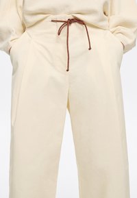 Pantaloni color crema con una vestibilità rilassata, realizzati in un tessuto testurizzato, con tasche laterali e un cordoncino marrone in vita.