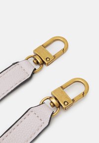 Skórzany pasek w jasnoróżowym kolorze z czarną krawędzią, wyposażony w mosiężne okucia i obrotowe klipsy. Gładka tekstura i minimalistyczne detale wzornicze.