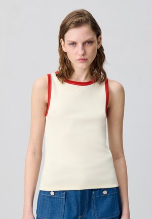 Top in crema con rifiniture rosse a costine lungo lo scollo e le armature, caratterizzato da un design aderente e una texture morbida. Dettaglio minimalista.