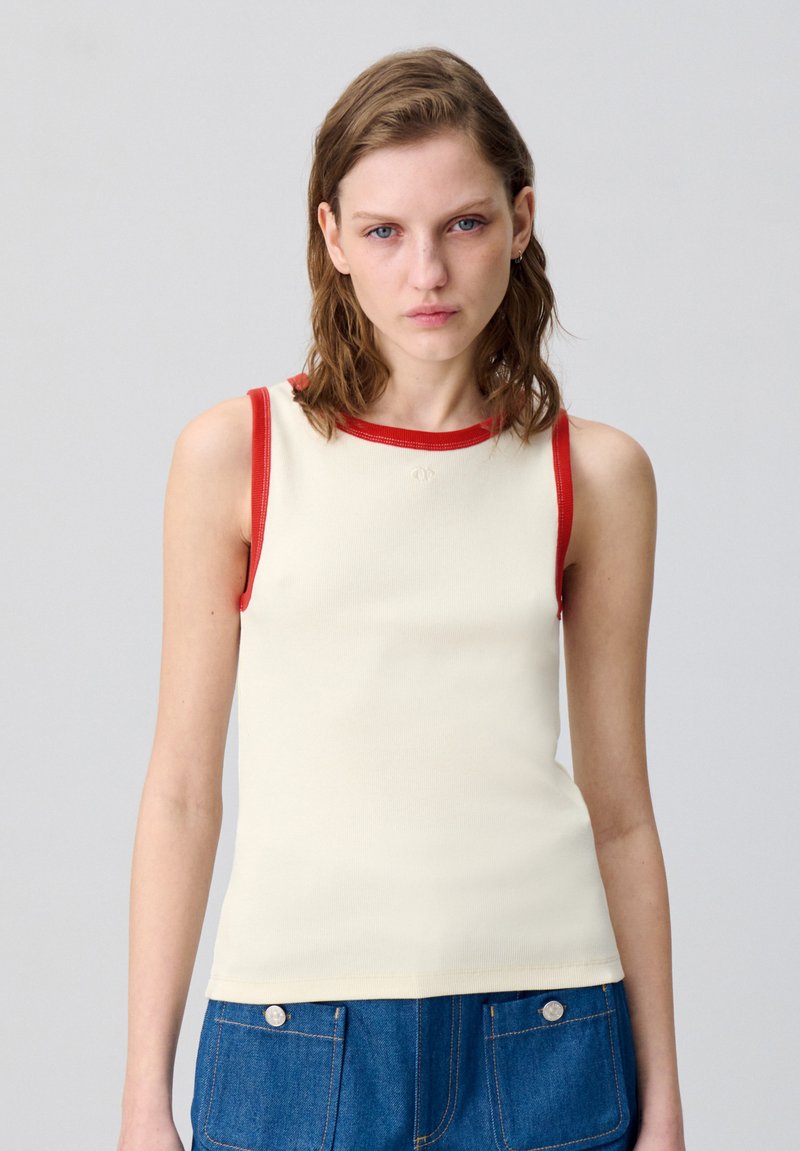 Top in crema con rifiniture rosse a costine lungo lo scollo e le armature, caratterizzato da un design aderente e una texture morbida. Dettaglio minimalista.