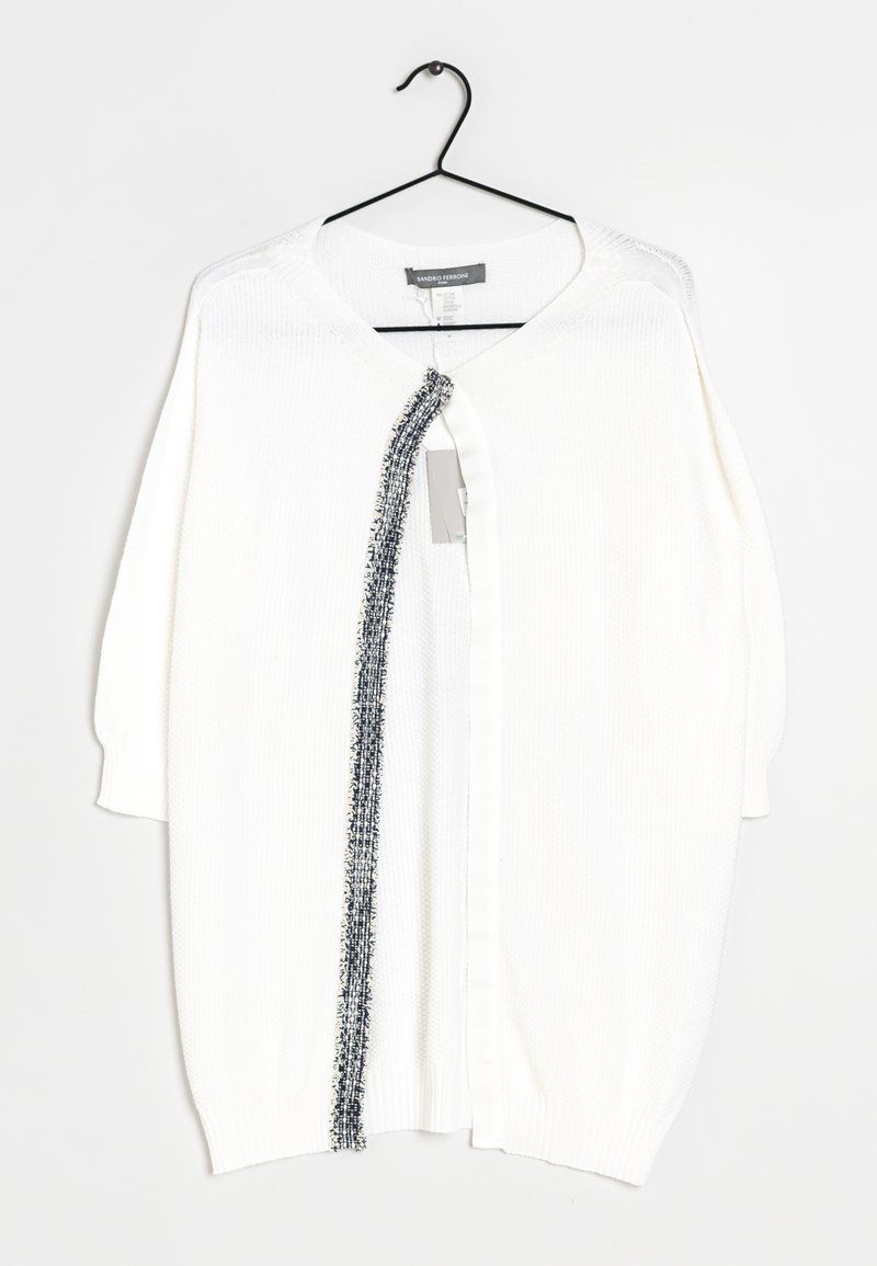 Biały dziergany kardigan z opuszczonymi ramionami, z kontrastową teksturowaną czarną lamówką wzdłuż przedniego otwarcia. Zawieszony na czarnym haczyku.