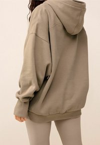 Oversized bluza z kapturem w stonowanym oliwkowym kolorze. Posiada prążkowane mankiety i dół, miękką teksturę oraz luźny krój.