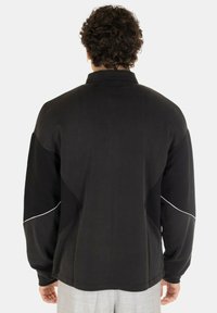 Pullover nero con colletto alto, dotato di pannelli laterali testurizzati a contrasto, maniche lunghe e piping bianco sugli spallacci.