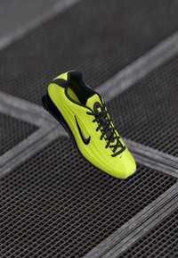 Erkkollane ja must Nike spordijalats paeltega, asetatud linnakeskkonnas metallv�õrgupinna kohale.