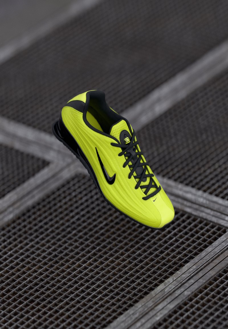 Erkkollane ja must Nike spordijalats paeltega, asetatud linnakeskkonnas metallvõrgupinna kohale.