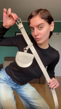 White leather belt with a small, curved crossbody pouch. Features a gold-tone buckle, embossed texture, and adjustable strap.