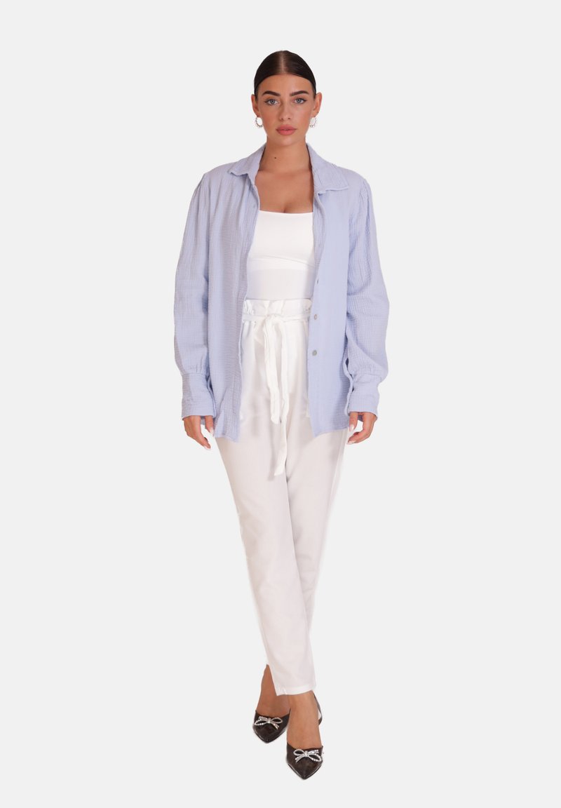 Camicia azzurra chiaro a maniche lunghe, indossata sopra un top bianco aderente e pantaloni bianchi a pieghe. Scarpe nere con punta a punta e fiocchi.