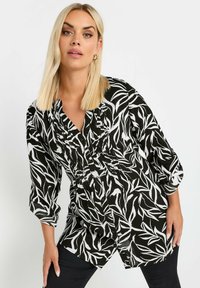 Blusa a righe bianco e nero con maniche a tre quarti, chiusura con bottoni sul davanti e dettagli arricciati. Tessuto leggero con una texture liscia.
