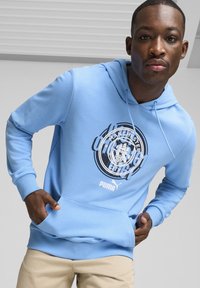 Svetlo modra kapuca iz mehkega materiala, s krožnim logotipom Manchester City na sredini, kenguru žepom in rebrastimi zapestji.