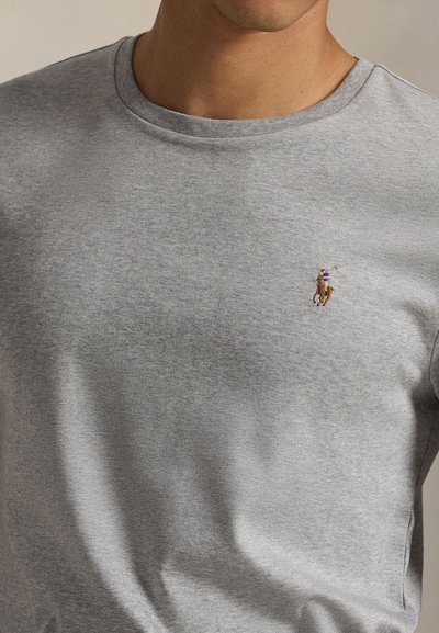 Prikaz osobe koja nosi svijetlo sivu majicu s okruglim izrezom s malim izvezenim logotipom igrača pola na konju na lijevoj strani prsa.