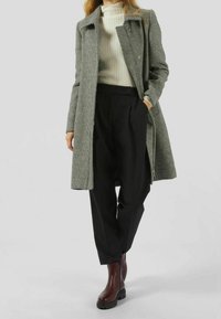 Abrigo de patrón de espiga en blanco y negro, con un diseño entallado, que lleva un suéter de canalé ligero y pantalones negros de cintura alta. Botines marrones.