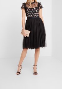 Robe noire avec un design floral brodé, corsage transparent, jupe en tulle et manches volantes. Accompagnée d'une pochette rose pâle.