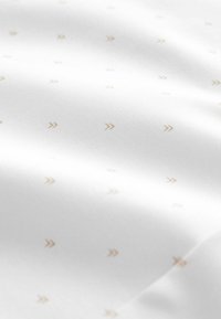Textil mit einem weißen Stoff, der ein dezentes Muster aus kleinen, goldenen Pfeilen aufweist, die gleichmäßig verteilt sind. Der Stoff hat eine glatte Textur und einen leichten Glanz.
