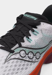 Κοντινό πλάνο λευκού αθλητικού παπουτσιού Saucony με μαύρα κορδόνια, τιρκουάζ ρουθούνια και πορτοκαλί άκρη στη σόλα.