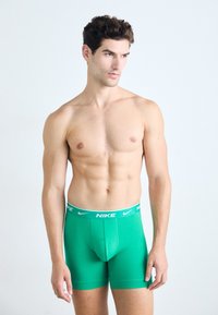 Groene katoenen boxershorts met een strakke pasvorm en een witte Nike-logo- tailleband. Zachte textuur, lengte tot halverwege de dij, zonder extra patronen of accenten.