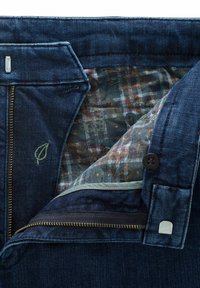 Jean en denim avec la fermeture éclair partiellement ouverte, montrant la doublure intérieure à motif floral, la fermeture éclair, le bouton et un petit détail brodé de feuille sur la taille.