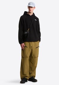 Μαύρο φλις φούτερ με κουκούλα, κίτρινο παντελόνι καρό με φερμουάρ, μαύρη τσάντα χιαστί, ανοιχτό μπλε καπέλο και μαύρα παπούτσια με υφασμένα πέλματα.