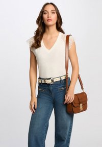 Top bianco a coste con dettagli in pizzo sulle spalle, abbinato a jeans blu in cotone a vita alta e una borsa a tracolla in pelle marrone.
