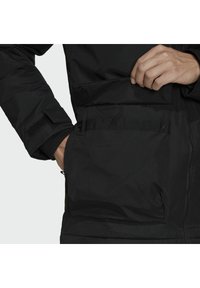 Černá vycpaná bunda s přední kapsou se klopou, suchým zipem na rukávu a hladkou texturou, navržena pro teplo.