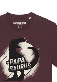 Bordeauxrotes Baumwoll-T-Shirt mit einem schwarzen Dinosaurier-Graphic und dem Text "PAPA SAURUS" in fetter, abgenutzter Schrift auf hellen Hintergrund.
