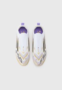 Scarpe da ginnastica bianche con un design elegante, caratterizzate da accenti neri, dettagli dorati e un interno viola. Il testo "F50" è visibile sul lato.