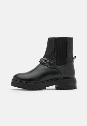 Zwarte leren enkellaars met chunky zool, elastisch zijpaneel, treklus aan de hiel en decoratieve metalen ketting over de voorkant.