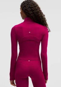 Kitsas pikk-käistega särk erksas roosas, valmistatud venivast kangast. Omab kõrget kraed ja diskreetset logo detaili, mis asub selja keskosas.