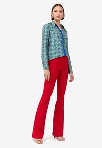 Camicia a maniche lunghe a fantasia in blu e verde con bottoni sul davanti, abbinata a pantaloni rossi a zampa d'elefante e décolleté argentati con fascia.