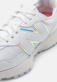 White sneaker with mesh and leather materials, featuring a colorful iridescent accent, round toe, and textured rubber sole.