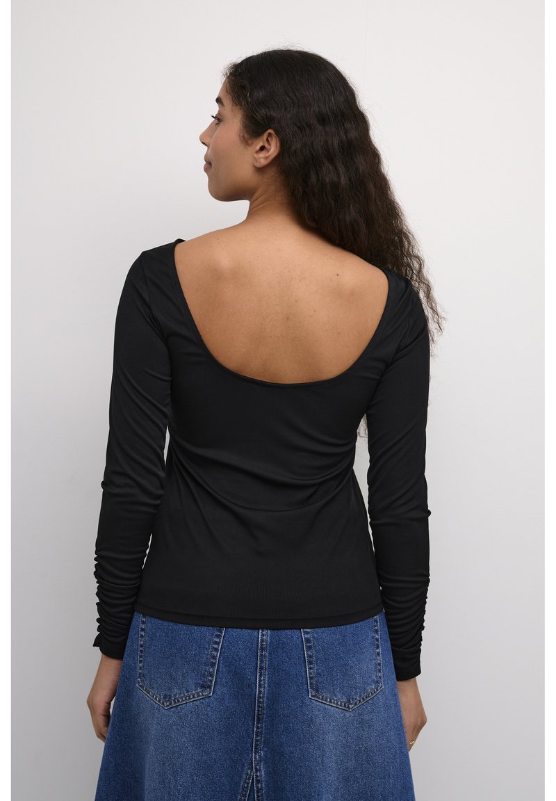 Schwarzes Langarmoberteil mit einem tiefen Rückendesign, aus geripptem Material gefertigt. Kombiniert mit einem Denim-Rock mit Taschen und strukturiertem Saum.