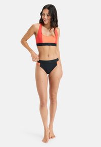 Completo bikini arancione e nero; include un top sportivo con spalline spesse e fascia con logo, e slip a vita alta con dettagli colorati.