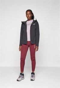 Svart huva jacka, ljusrosa t-shirt med "TERREX"-logotyp, vinröda leggings och gråsvarta vandringsskor. Släta texturer, åtsittande design.